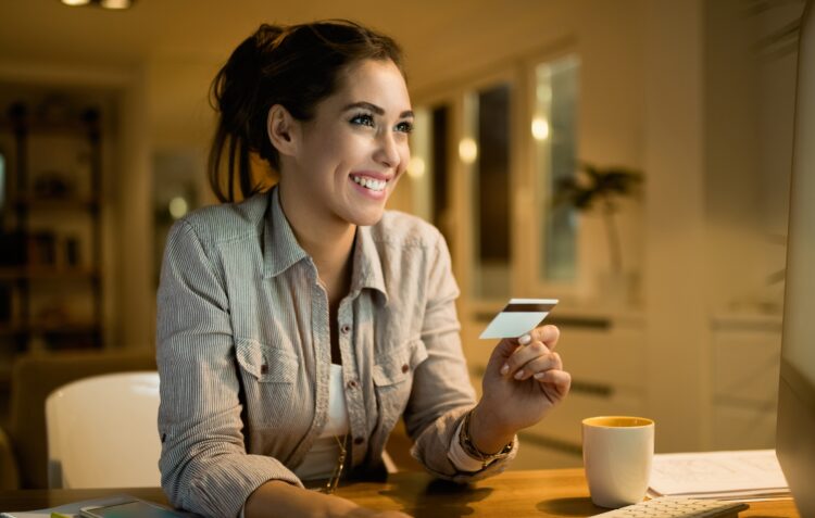 Happy woman using credit card for online banking at night at home.