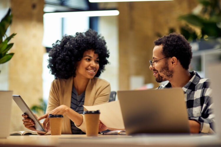 Sharing fresh ideas. Two young happy multiracial business people sitting at desk and communicating while working together in coworking space. Office life, teamwork and business